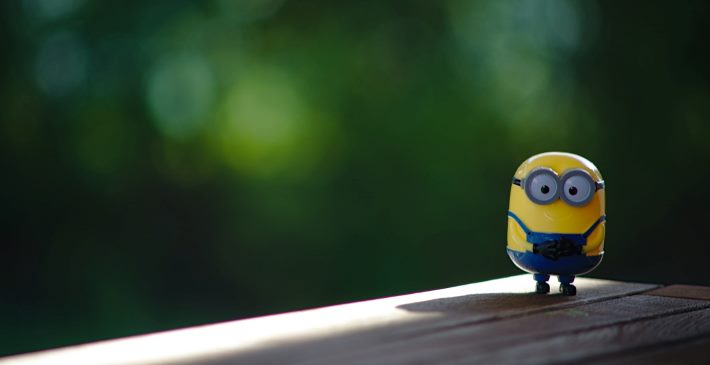 A photo of a lone minion toy standing in an anticpatory state in a shadow adjacent to sunshine